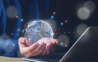 Identity Threat Prevention. A person cupping a holographic globe of Earth over an open laptop. The scene is surrounded by glowing digital particles, evoking a sense of global connectivity, cloud technology, or digital transformation.