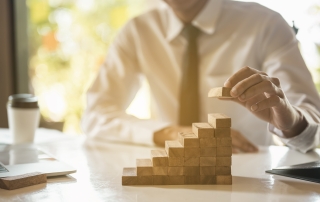 Businessman hand pulling out or placing wood block on the tower and semi-pyramid in modern office. Plan and strategy in business.