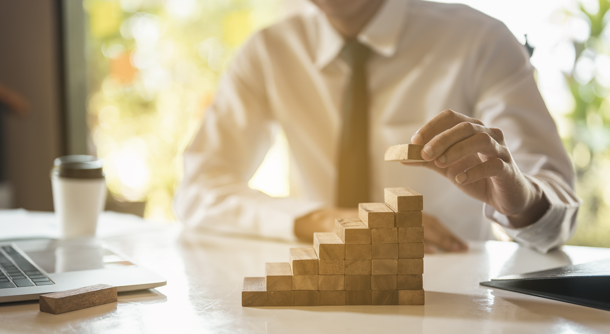 Businessman hand pulling out or placing wood block on the tower and semi-pyramid in modern office. Plan and strategy in business.