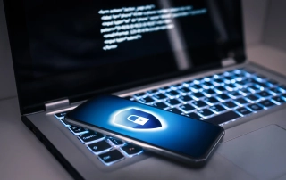 Cyber breach management services. The image shows a smartphone resting on top of a laptop with unreadable inscription. The smartphone has an icon of a lock on a shield shown on its screen.