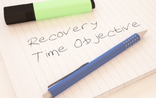 Recovery Time Objective. The image shows a lined notebook page with the handwritten phrase "Recovery Time Objective." A blue pen and a green highlighter are placed on the notebook, adding a casual yet purposeful feel to the setting. The phrase "Recovery Time Objective" emphasizes the importance of setting goals for system recovery after disruptions, a concept often used in business continuity and disaster recovery planning. The items suggest a planning or brainstorming session focused on determining acceptable downtime limits.