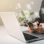 Responding to DarkSide ransomware threat. The image shows a person holding a smartphone while sitting in front of an open laptop. There are digital icons floating around the person, symbolizing various elements related to cybersecurity. These icons include a shield with a padlock in the center, folder icons with locks, and other data security symbols, all of which represent the secure handling of information. The person is dressed in business attire, with only their hands and part of their torso visible. The overall scene emphasizes the connection between mobile and computer security.