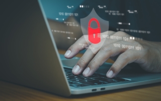 Handling REvil ransomware attack. This image shows a close-up of a person’s hands typing on a laptop keyboard. Overlaid on the image is a graphic representation of cybersecurity, featuring a red padlock icon set against a transparent shield shape. The padlock symbolizes security, and binary code (sequences of ones and zeros) is displayed floating in the background, further emphasizing the concept of digital protection. The overall tone of the image is serious and professional, with a dark, muted color scheme to evoke themes of technology and cybersecurity.