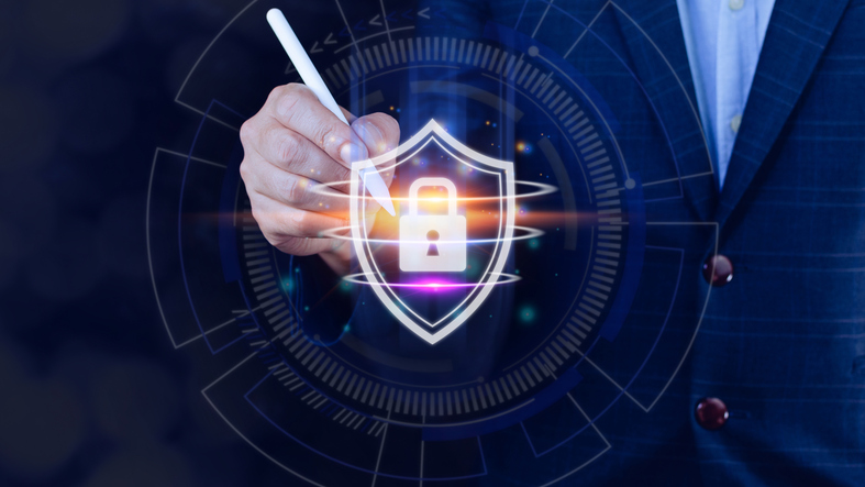 Insider threats and ransomware risks. A person in a suit holds a stylus or pen pointing toward a glowing digital shield with a lock icon at its center. The background has a high-tech, circular interface design, emphasizing the theme of cybersecurity and data encryption.