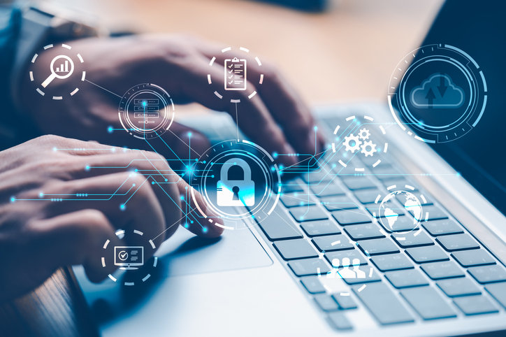 Machine learning for ransomware prevention. Hands are typing on a laptop keyboard with a futuristic digital overlay. The overlay features glowing blue security icons, including a padlock, gears, and cloud symbols, signifying online security, system settings, and cloud data protection.