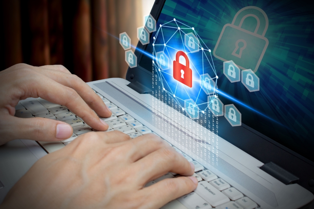 Protecting against Clop ransomware. This image shows a close-up of hands typing on a laptop keyboard, symbolizing human interaction with technology. Overlaid on the screen is a prominent red padlock surrounded by a digital network, represented by a web of glowing hexagonal nodes connected by white lines. This visual represents cybersecurity and data protection. In the background, the laptop screen displays larger, semi-transparent padlock icons and a blue digital glow, emphasizing the theme of security in the digital space. The image uses contrasting warm tones for the hands and neutral background with cool tones of blue and red for the digital elements, creating a striking focus on cybersecurity and data safety.