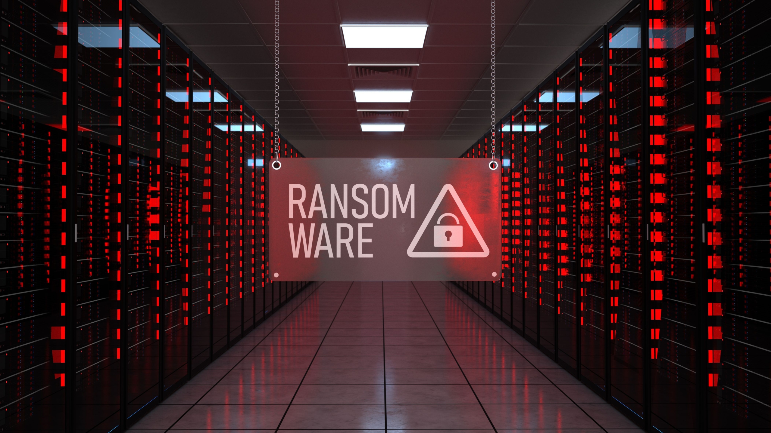 Recovering from Netwalker ransomware attack. This image depicts a data center with rows of server racks illuminated by red lights, creating an intense and alarming atmosphere. Hanging in the center of the image is a translucent sign displaying the word "RANSOMWARE" in bold white letters, accompanied by a warning triangle icon with a padlock inside it. The perspective draws attention to the central aisle, which is well-lit and contrasts with the red glow of the servers, emphasizing the theme of cybersecurity threats and the urgency of ransomware attacks. The overall mood is stark and ominous, fitting for the subject of digital vulnerabilities.