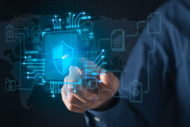 Disaster Recovery as a Service (DRaaS). A close-up of a hand reaching towards a floating digital interface that displays a shield with a checkmark at its center. The background includes a futuristic, circuit-like design with interconnected symbols such as a database, a house, and bar graphs, suggesting data security and protection.