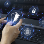 IoT device security from ransomware attacks. A pair of hands hovers over a laptop keyboard, with holographic icons floating above the screen. These icons include a shield symbolizing cybersecurity, a fingerprint for biometric authentication, a padlock for security, and a globe representing internet connectivity.