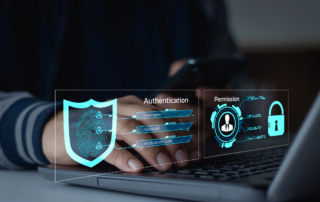 Human error in ransomware attacks. A person is typing on a laptop keyboard, with their hands partially visible. Overlaid on the image is a futuristic digital authentication interface, featuring a glowing blue shield with a fingerprint-like circuit design inside. The interface displays "Authentication" with fields for Username, Password, and Verification Code, emphasizing secure login procedures. To the right, another panel labeled "Permission" shows a user profile icon and a padlock, symbolizing access control and data security. The background is blurred, creating a high-tech, cybersecurity-themed aesthetic focused on identity verification and secure access.