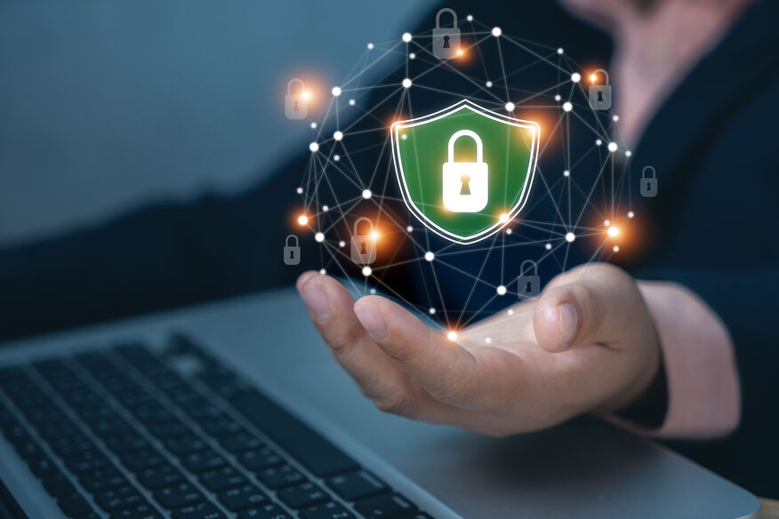 Network traffic monitoring for ransomware. A person in a business suit extends their hand, and above it, a floating green shield with a padlock is surrounded by interconnected nodes and glowing padlock icons. The background features a laptop, emphasizing cybersecurity and network protection.