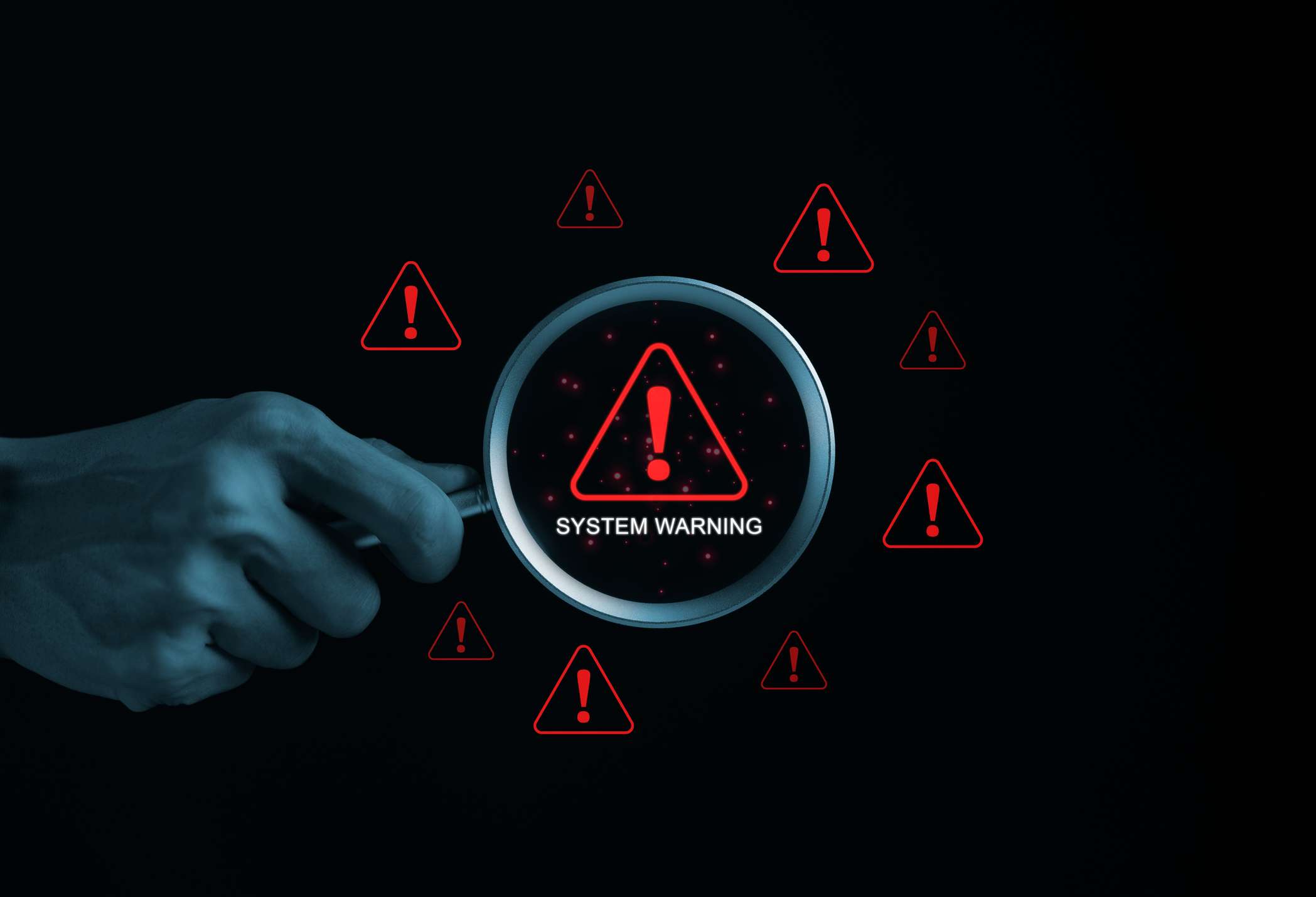 Data loss prevention in ransomware defense. A hand holding a magnifying glass is examining a screen filled with red exclamation marks inside warning triangles. The text "System Warning" is displayed in the center, indicating a critical error, vulnerability, or cybersecurity alert. The background is black with a hacker-style digital threat environment, emphasizing cybersecurity risks.