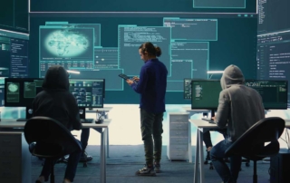 Advanced Email Security Protection. Three people are working in a high-tech command center. They face multiple monitors displaying digital blueprints, data streams, and global threat visuals. The middle person stands while using a tablet; the others sit and appear focused on their work. The overall feel is high-intensity and cyber-operations focused.