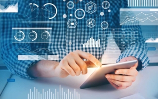 Email Phishing Defense Solutions. A person in a blue and white checkered shirt is seated at a desk, using a tablet with both hands. Floating over the image are bright digital graphics: pie charts, bar graphs, hexagonal icons, and financial data overlays. It gives the impression of someone analyzing data or using business intelligence tools in a futuristic digital workspace.