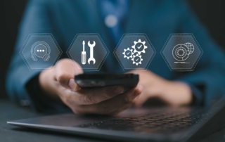 Preventative Software Patching Services. A close-up of a person using a smartphone in front of a laptop. Overlaid on the image are transparent icons representing tech support tools: a headset, screwdriver and wrench, gears with check marks, and a globe with a gear—symbolizing digital infrastructure or IT service support.