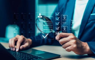 API security ransomware prevention. A person in a suit holds a magnifying glass over a digital checklist interface while typing on a laptop. Digital icons representing documents and approvals float in the air, symbolizing inspection, audit, or verification processes.