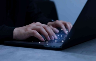 Email Security for Regulatory Compliance. A minimalist photo showing hands typing on a sleek black laptop in a dark setting. The lighting is low, with only the faint glow from the screen, creating an atmosphere of quiet focus, possibly during late-night cybersecurity monitoring or analysis.