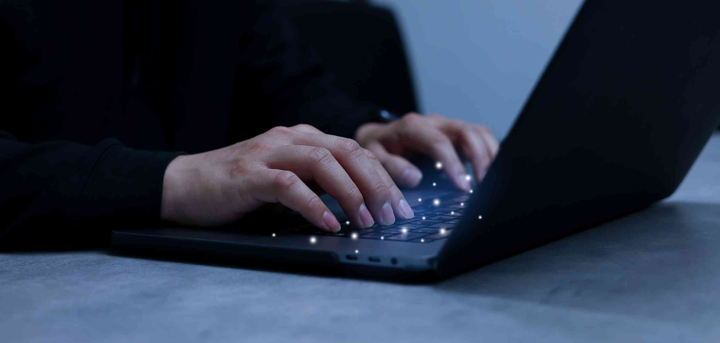 Email Security for Regulatory Compliance. A minimalist photo showing hands typing on a sleek black laptop in a dark setting. The lighting is low, with only the faint glow from the screen, creating an atmosphere of quiet focus, possibly during late-night cybersecurity monitoring or analysis.