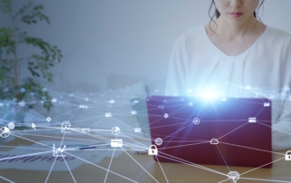 Patch Deployment Automation. A woman sits at a desk using a tablet, partially obscured by a bright digital overlay of interconnected icons such as locks, clouds, and gears. The imagery represents digital security and network communication.