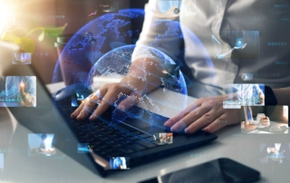 IT team ransomware training. A person in a white shirt works on a laptop, surrounded by holographic globes and floating images of people and graphs.