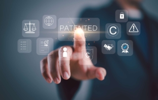 Immutable Architecture for Ransomware. A person pointing at a virtual screen displaying icons related to intellectual property—like a padlock, copyright symbol, checkmark, balance scale, and the word “PATENTED.” The background is dark with a business attire silhouette.